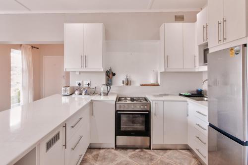 a white kitchen with white cabinets and a stove at Amblewood Beach Cottages in Kenton on Sea