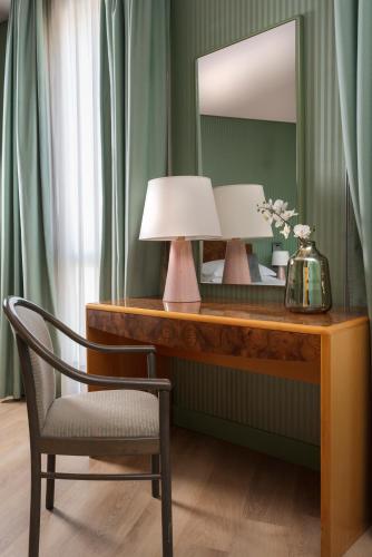 a table with two lamps and a chair and a mirror at Perugia Park Hotel in Perugia