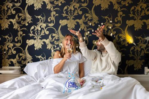Un uomo e una donna stesi a letto con bicchieri da champagne di Amsterdam Canal Hotel ad Amsterdam