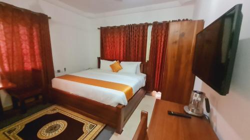 Schlafzimmer mit einem Bett, einem Schreibtisch und einem TV in der Unterkunft Bassi Hotel in Takoradi