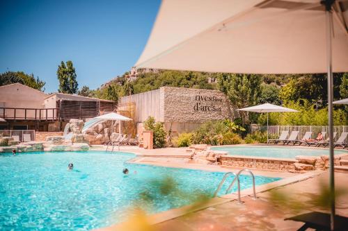 a swimming pool with an umbrella and people in it at Rives d'Arc in Vallon-Pont-dʼArc