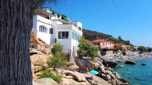 a white building on a rocky beach with people in the water at Casa Pomonte in Pomonte