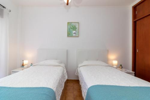 カルヴォエイロにあるApartment Farolの白い壁と青いシーツが備わる客室のベッド2台