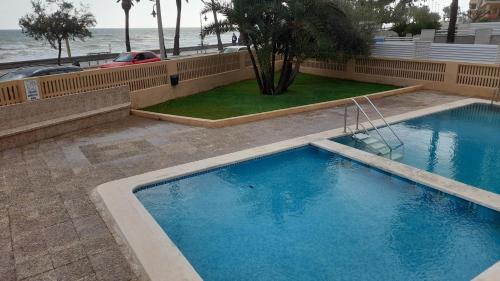 een groot blauw zwembad naast het strand bij Apartamanto FRENTE AL MAR, un dormitorio con dos camas, mas otra cama abatible en el salon in Benicàssim