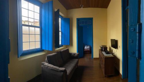 Casa estilo colonial, no Centro de Aiuruoca-MG. في أيوريوكا: غرفة معيشة مع أريكة ونوافذ زرقاء