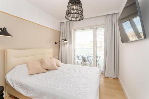 a white bedroom with a bed and a balcony at Aqua Polanki Bodnar Apartments in Kołobrzeg
