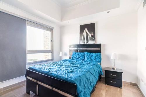 ein Schlafzimmer mit einem Bett mit blauer Decke und einem Fenster in der Unterkunft Luxurious 2BDR condo located in Prestigious Tower. in Santo Domingo