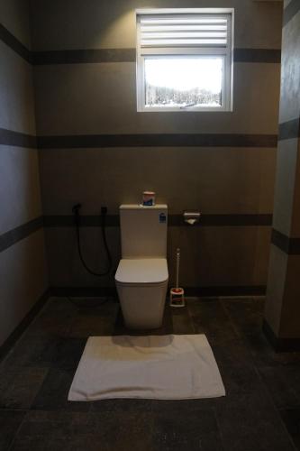 a bathroom with a toilet with a window and a white rug at Turtle Bay Beach Resort in Mirissa