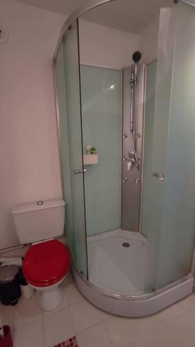 a bathroom with a shower and a toilet with a red seat at Studio Ouistreham entre centre-ville et plages in Ouistreham
