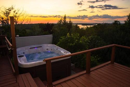 a hot tub on a deck with the sunset in the background at Cozy Sunset Cottage Overlooking Rice Lake in Roseneath