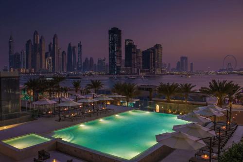 杜拜的住宿－Radisson Beach Resort Palm Jumeirah，一个带遮阳伞的游泳池,晚上则享有城市天际线