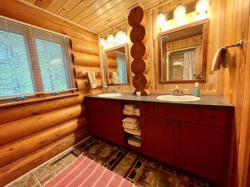 La salle de bains en rondins est pourvue de 2 lavabos et d'un miroir. dans l'établissement Camp Voyager Log Cabin resort pool, golf, trails, lakes more, à Webb Lake
