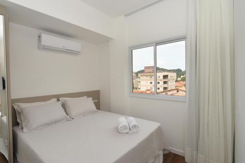 a white bedroom with a bed and a window at Vila do Centro Apart Hotel in Bombinhas