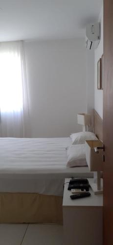 um quarto com uma cama branca e uma janela em Residencial Iloa na Barra de São Miguel