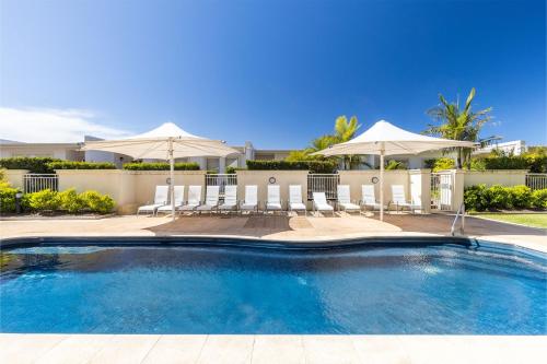 a swimming pool with chairs and umbrellas in a yard at 203 The Breakwater 2 Messines St magical unit with lift pool views and aircon in Shoal Bay