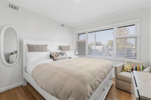 a white bedroom with a large bed and a chair at On The Beach in Rosebud