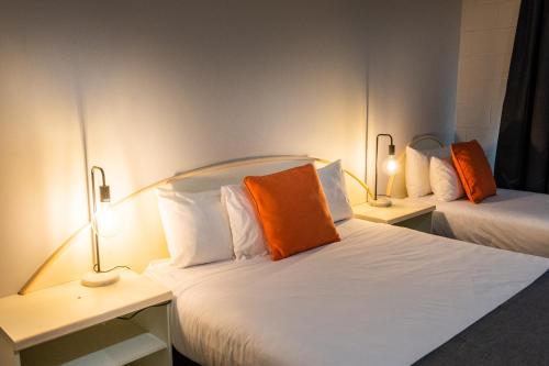 two beds with orange pillows in a room at River Motel in Queanbeyan
