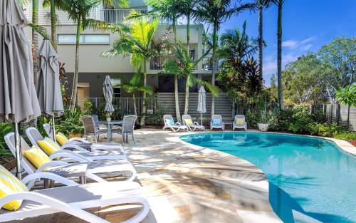a swimming pool with white chairs and a hotel at Metzo Noosa Resort in Noosaville