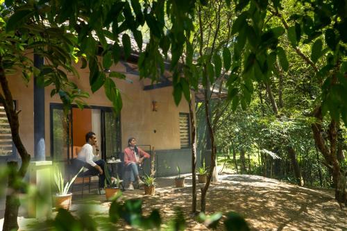 two men sitting on a bench in front of a house at Klov Resort & Spa in Wayanad