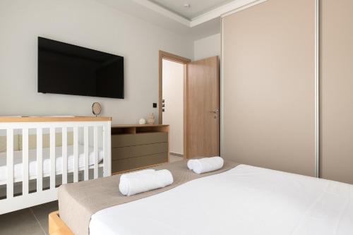 a white bedroom with a crib and a flat screen tv at Mirena Luxury Living-Casa di Maria in Afantou