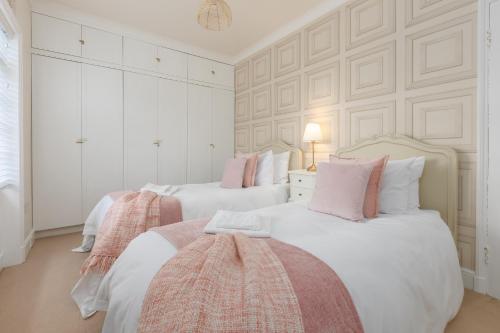 two beds in a bedroom with white walls and pink pillows at Charles Alexander Short Stay - Rose Cottage in Lytham St Annes