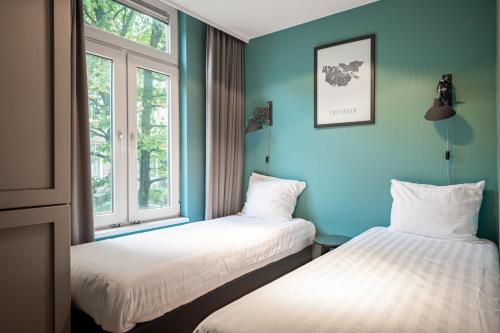 Dos camas en una habitación con paredes y ventanas azules. en Musea Hotel & Apartments, en Ámsterdam