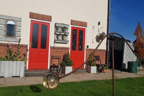 a house with red doors and a clock in the yard at Peaceful self contained Studio in lovely garden. in Hinckley