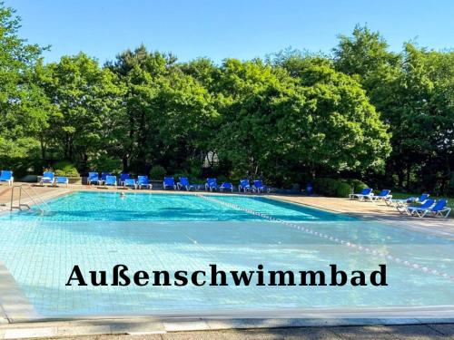 a swimming pool with blue chairs and trees at Top - Seaside Appartement mit Meerblick in Timmendorfer Strand