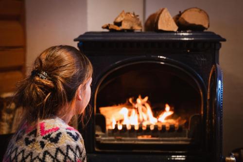a woman is sitting in front of a fireplace at Rondane River Lodge - Rondane Gjestegård in Enden