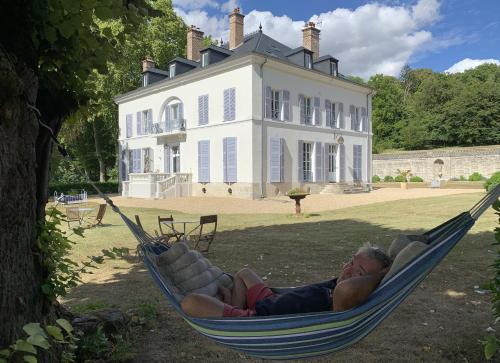 a man laying in a hammock in front of a house at La Grande Maison in Seine-Port