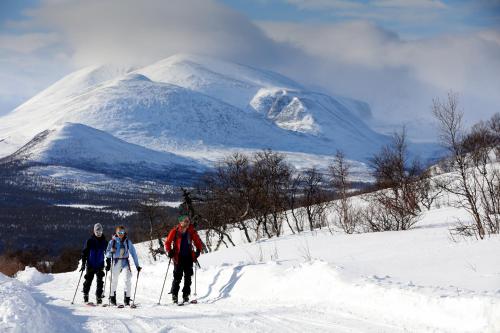 three people on skis in the snow in front of a mountain at Rondane River Lodge - Rondane Gjestegård in Enden