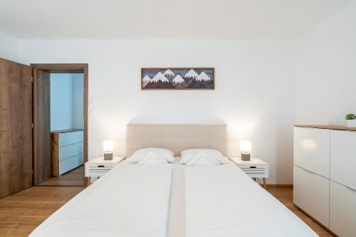 a white bedroom with a large white bed with two lamps at Apartmány Oravskie in Zuberec