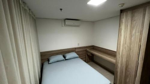 a small room with a bed with two blue pillows at Flat Brookfield Towers 2309 in Goiânia
