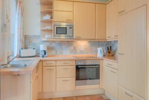 a kitchen with wooden cabinets and a sink and a microwave at Strandhaus Thiessow Whg_ 1 in Thiessow