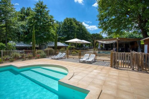 a swimming pool with two lounge chairs and an umbrella at Camping du Lac de Grolejac in Groléjac