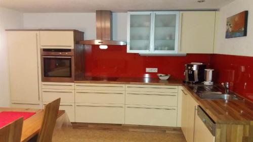 a kitchen with white cabinets and a red wall at Loretz Luzia in Silbertal