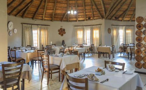 un comedor con mesas y sillas blancas y ventanas en Nongoma Lodge & Inn CC, en Nongoma