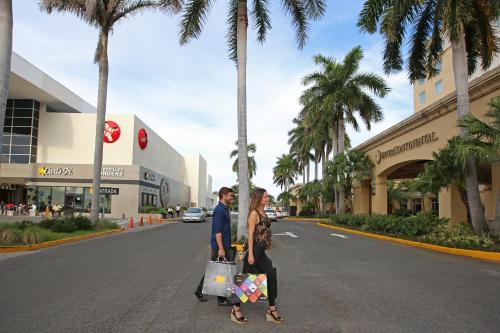 Real Intercontinental Metrocentro Managua, an IHG Hotel في ماناغوا: رجل وامرأة يسيران في الشارع ومعهم حقائب تسوق