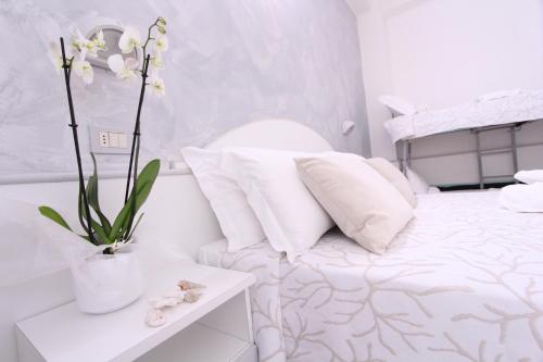 ミザーノ・アドリアーティコにあるHotel Lidoの白い枕と花のベッドが備わる白いベッドルーム1室が備わります。