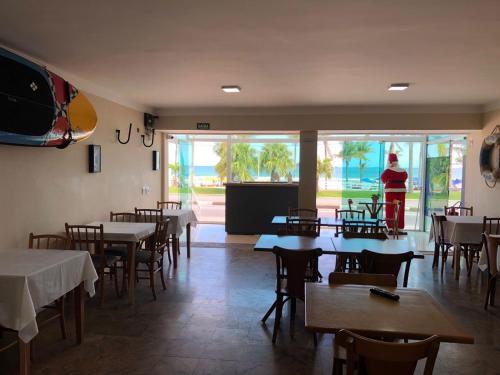 a restaurant with tables and chairs and a woman standing in the background at HOTEL ENSEADA BEIRA MAR in Guarujá