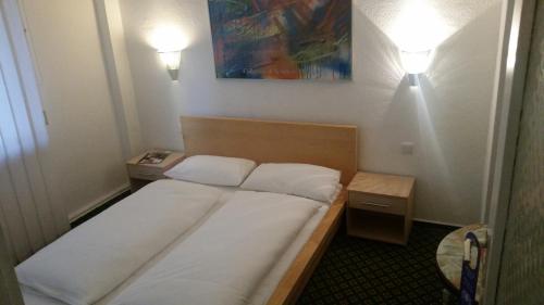 a bed in a small room with two lights on at Hotelgarni Frankfurt in Frankfurt/Main