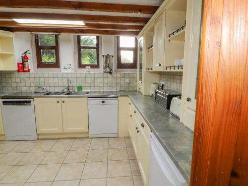 a large kitchen with white cabinets and a sink at Old School Muncaster House in Ravenglass