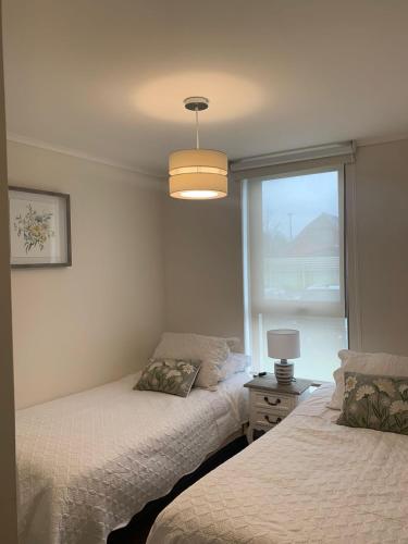 two beds in a room with a window and a lamp at Bienvenidos a Valdivia in Valdivia