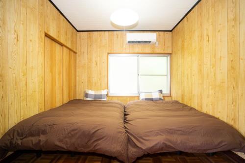 uma cama num quarto com paredes de madeira e uma janela em I,K,I HOUSE TSURUKIFURE - Vacation STAY 14773v em Iki