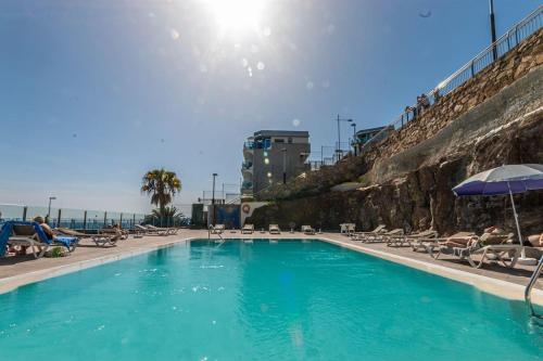 a swimming pool with chairs and umbrellas and the ocean at Golden Sunny View Apartment in Puerto Rico de Gran Canaria