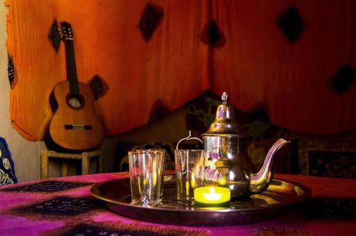 une bouilloire et des verres sur une table avec une guitare dans l'établissement LA PETITE MAISON DU LAC IRIKI, à Foum Zguid