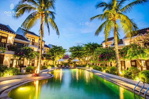 een zwembad in het midden van een resort met palmbomen bij Hoi An Coco River Resort & Spa in Hội An