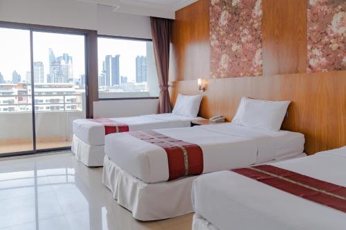 a hotel room with three beds and a large window at Forum Park Hotel in Bangkok