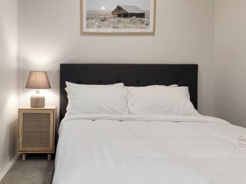 a white bed with a black headboard next to a lamp at Brand new stylish 2BR apartment- free parking in Auckland