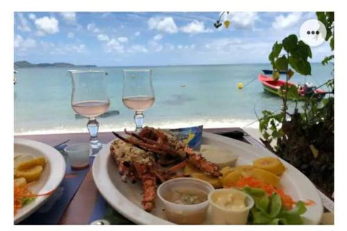a plate of food with two glasses of wine and the ocean at Superbe appartement cosy neuf in Grand Case